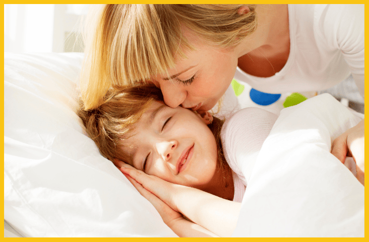 Creating a positive morning routine A guide for smooth starts with children blog feature image mother kissing her child and they lay in a bed with white sheets.
